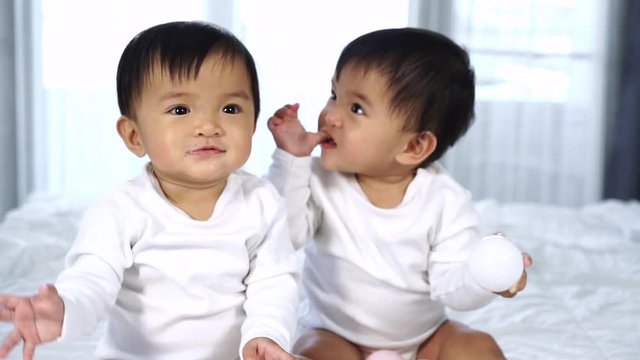 slow-motion of cheerful twin babies playing color ball on a bed