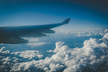 Fototapeta na wymiar Wing of large passenger jet in mid flight above fluffy clouds and distand earth