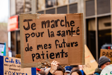 Environmentalists march for change. A French sign is seen closeup saying i'm walking for the health of my future patients as ecological demonstrators protest in an urban city street.
