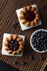 Homemade sweets. Yummy cakes with jam and wild bilberries on ribbed oak cutting board top view copy space. Low key still life with natural lighting