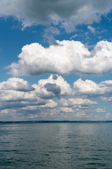 vertical background of flat anvil-like cumulus clouds in blue sky and blue lake below