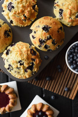 Freshly baked crumble muffins and cakes with wild bilberries on oak cutting board copy space. Low key still life with natural lighting