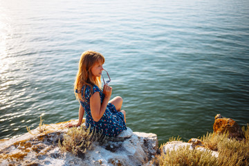 The girl in the blue dress on the stone sits by the sea