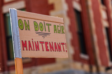 Ecological activist holds French placard. A closeup view of a French sign, saying we must act now, as environmental demonstrators gather in a city center to protest.