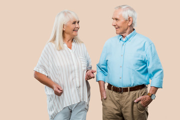 happy retired woman looking at husband and gesturing isolated on beige