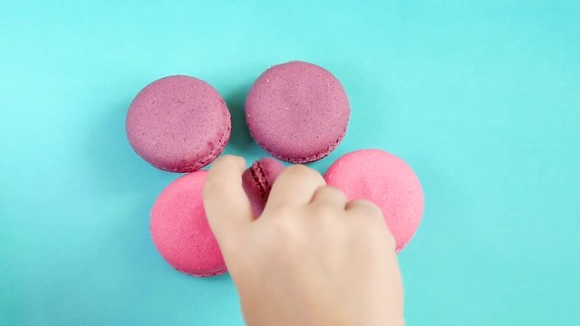 Beautiful bright desserts of macaroon lie on a blue background. The child's hand takes the cookies in slow motion.