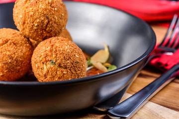 A serving of deep fried 'croquettes' in a dark colour bowl, on a red tomato sauce
