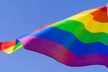 Gay rainbow flag waving in the wind in a clear blue sky