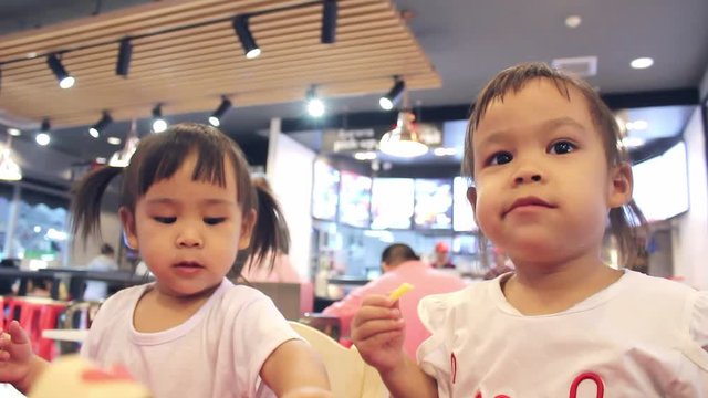 Happy Asian children are eating delicious French fries and drink some necta with her mother in restaurants.