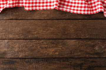 Red checkered tablecloth on wooden background. Top view