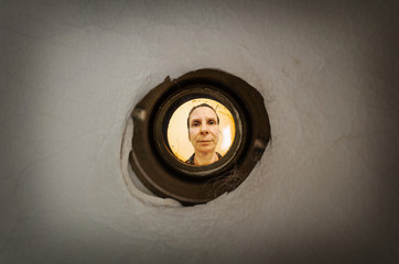 Woman seen out of focus through the old dirty peephole of the front door of a dark apartment