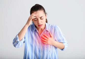 Young woman suffering from heart attack on light background