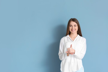 Young deaf mute woman using sign language on color background