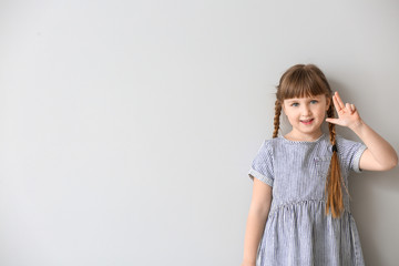 Cute deaf mute girl using sign language on light background