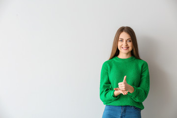 Young deaf mute woman using sign language on light background © Pixel-Shot
