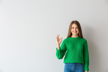 Young deaf mute woman using sign language on light background