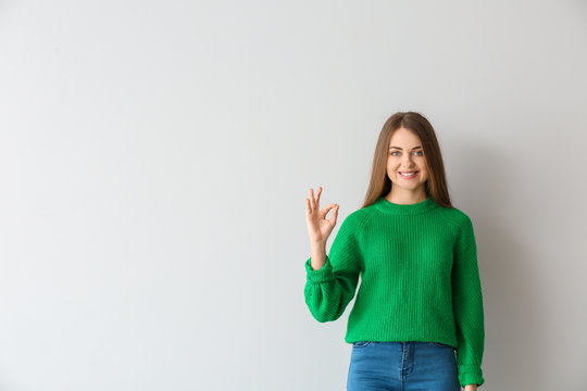 Young deaf mute woman using sign language on light background