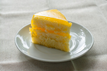 Delicious slice of orange cake served on white dish in coffee times on tablecloth.