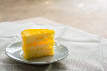 Delicious slice of orange cake served on white dish in coffee times on tablecloth.