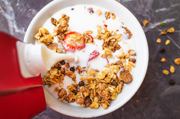 Muesli with chocolate and fresh strawberries on a dark gray background. Milk is poured into the plate. The concept of healthy breakfast, healthy eating. Flat lay, minimalism, top view. Place for text.