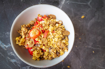 Muesli with chocolate and fresh strawberries in a plate on a dark gray background. The concept of healthy breakfast, healthy eating. Flat lay, minimalism, top view. Place for text.