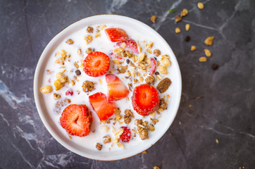 Muesli with chocolate and fresh strawberries with milk in a plate on a dark gray background. The concept of healthy breakfast, healthy eating. Flat lay, minimalism, top view. Place for text.