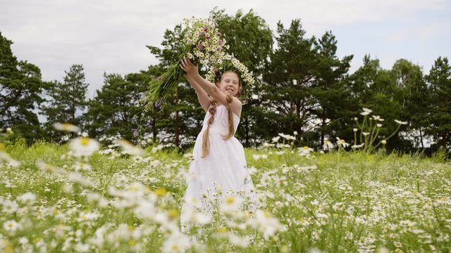 Girl Flowers Outdoor Blossom Daisy Meadow Scenery. Happy Attractive Caucasian Female Child in Floral Wreath Pose Picture. Cute Kid Enjoy Nature Hold Wildflowers Bouquet Leisure Concept