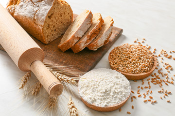 Rolling pin with fresh bread, wheat grains and flour on light background