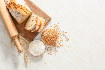 Rolling pin with fresh bread, wheat grains and flour on light background