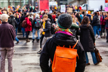 Environmentalists march for change. A woman is viewed from behind, wearing an orange backpack and...