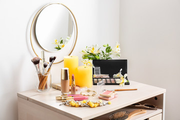 Makeup cosmetics with brushes and jewelry on dressing table in room