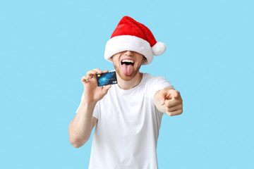 Fototapeta na wymiar Happy young man in Santa hat and with credit card on color background