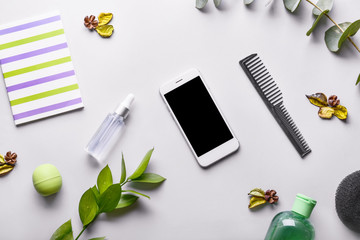 Mobile phone with cosmetics, notebook and comb on light background