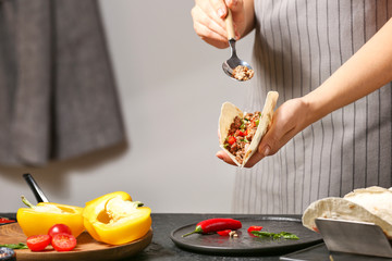 Woman preparing tasty fresh tacos in kitchen