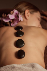 Beautiful young woman undergoing treatment with hot stones in spa salon