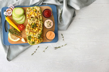 Board with tasty squash waffles, vegetables and sauces on white table