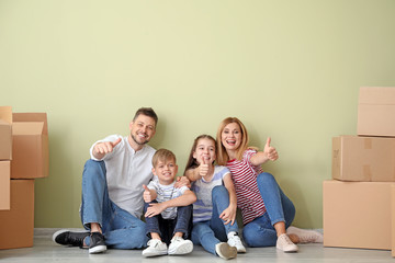 Happy family with belongings showing thumb-up gesture in their new house