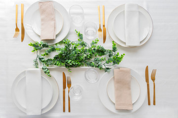Table setting for festive dinner with white porcelain plates, glasses, decorative textile and...