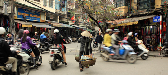Busy, bustling street intersection in Vietnam, with lots of traffic that includes people walking on foot, and commuting on bikes and scooters on the street - obrazy, fototapety, plakaty