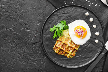 Plate with tasty squash waffle and fried egg on dark table