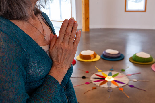 Old woman prays in meditation room. A closeup and side view on the wrinkled hands of an elderly spiritual lady, as she meditates close to the Native American color wheel.