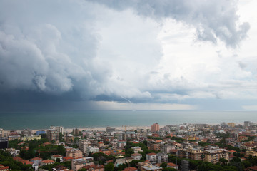 Storm with tornado in Rimini, Italy. Picturesque landscape view with sea, clouds, cityscape and whirlwind. Natural disaster. Mediterranean Sea.