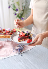 Obraz na płótnie Canvas Woman eating tasty chocolate strawberry cake in kitchen