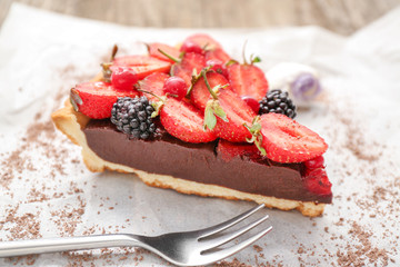 Piece of tasty chocolate strawberry cake on parchment, closeup