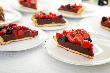 Plates with pieces of tasty chocolate strawberry cake on white table