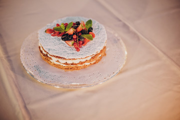 Beautiful simple wedding cake with fruits on table at wedding reception outdoors in the evening.Delicious little wedding cake in soft candle light in night.