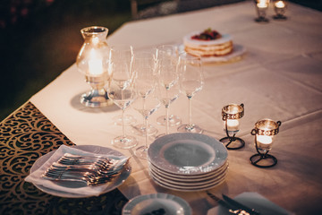 Wedding table with candles, cutlery and plates, champagne drink and glasses at reception outdoors in the evening. Luxury catering at  celebration in soft candle light. Christmas feast