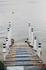 Beautiful old wooden dock with aged columns in white and blue colors on shore of Lago Maggiore in...
