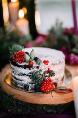 Delicate wedding white cake decorated with pomegranate and succulent surrounded by flowers and candles.
