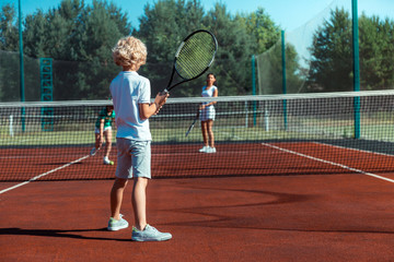Curly son holding tennis racket while playing tennis